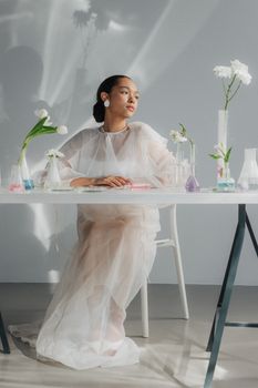 An elegant woman sits with glassware and flowers, blending science and art.