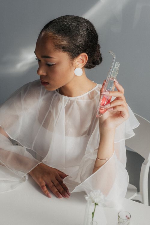 Free Woman in sheer attire holding a science flask with pink liquid, capturing elegance and curiosity. Stock Photo