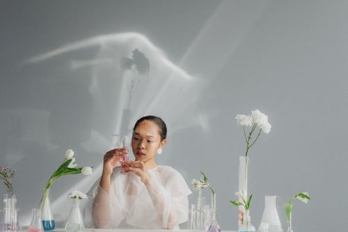 Free A woman in a lab holding a flask with plants, wearing protective clothing indoors. Stock Photo