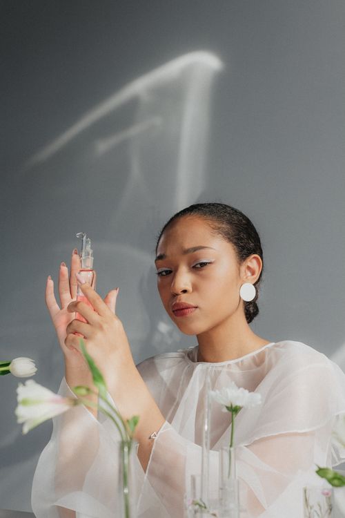 Free A stylish woman holds a flask amidst flowers, blending science with elegance. Stock Photo