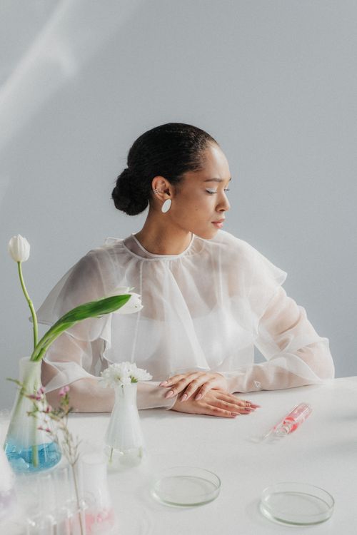 Free Woman in a sheer blouse sitting in a minimalist laboratory setting with glassware. Stock Photo