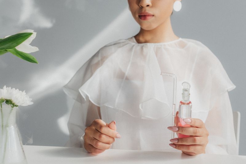 Woman in white blouse holding a glass flask in a minimalist laboratory environment.