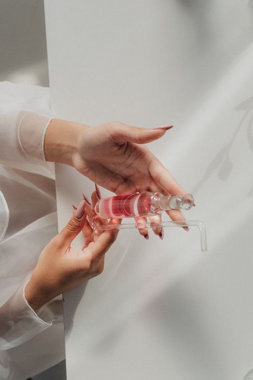 Free Close-up of hands carefully holding a glass flask with pink liquid in a lab setting. Stock Photo