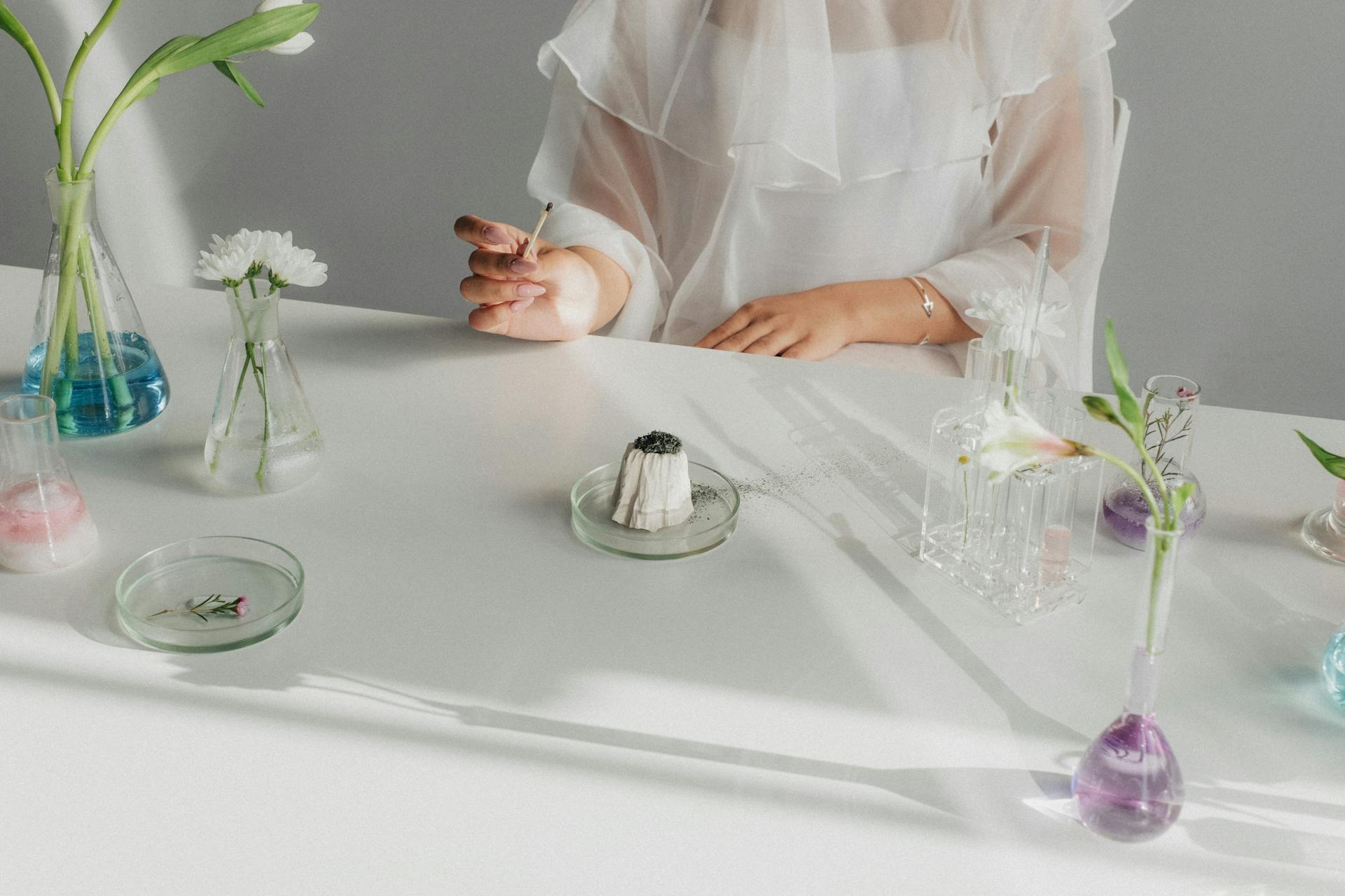 Elegant still life with various flowers in flasks on a white table, highlighting beauty and creativity in a serene atmosphere.