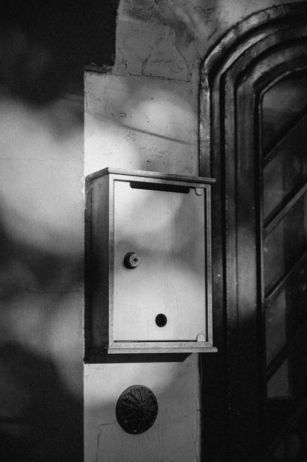 A grayscale image of a mailbox mounted on a wall, casting shadows.