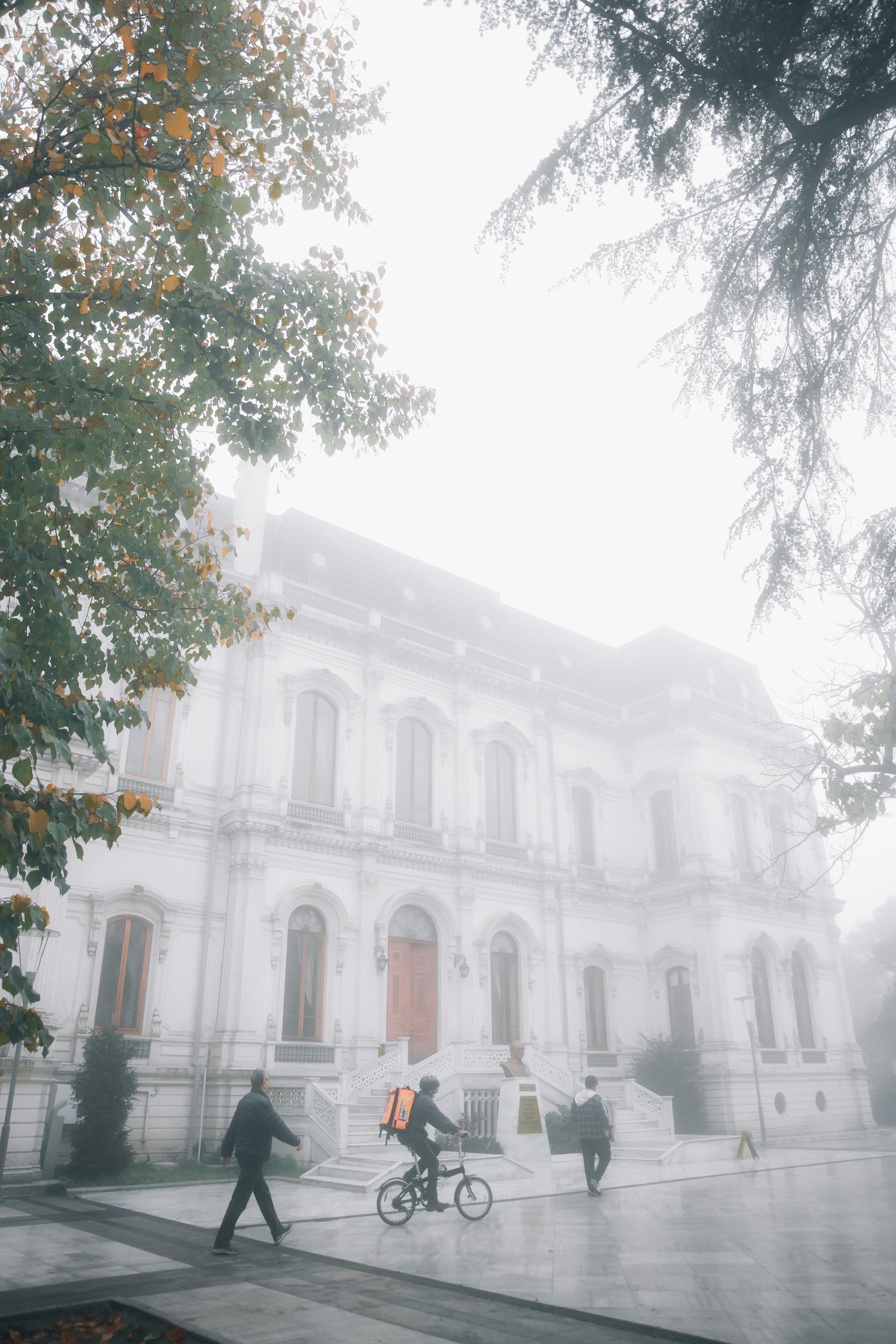 A misty morning scene of an Ottoman-style building in Istanbul, Turkey, with pedestrians and trees.