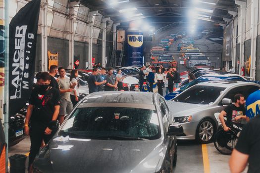 People gather indoors for a car meet featuring Mitsubishi Lancer Evolution in a garage setting.