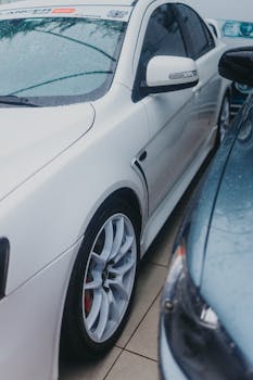 Close-up of sleek white car with rain droplets on windshield and tire.
