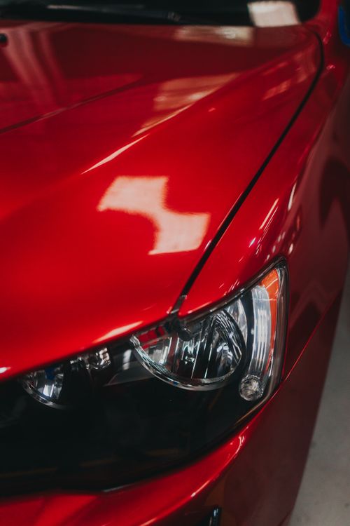 Free Detailed shot of a red car's metallic hood and sleek headlight, showcasing automotive design. Stock Photo