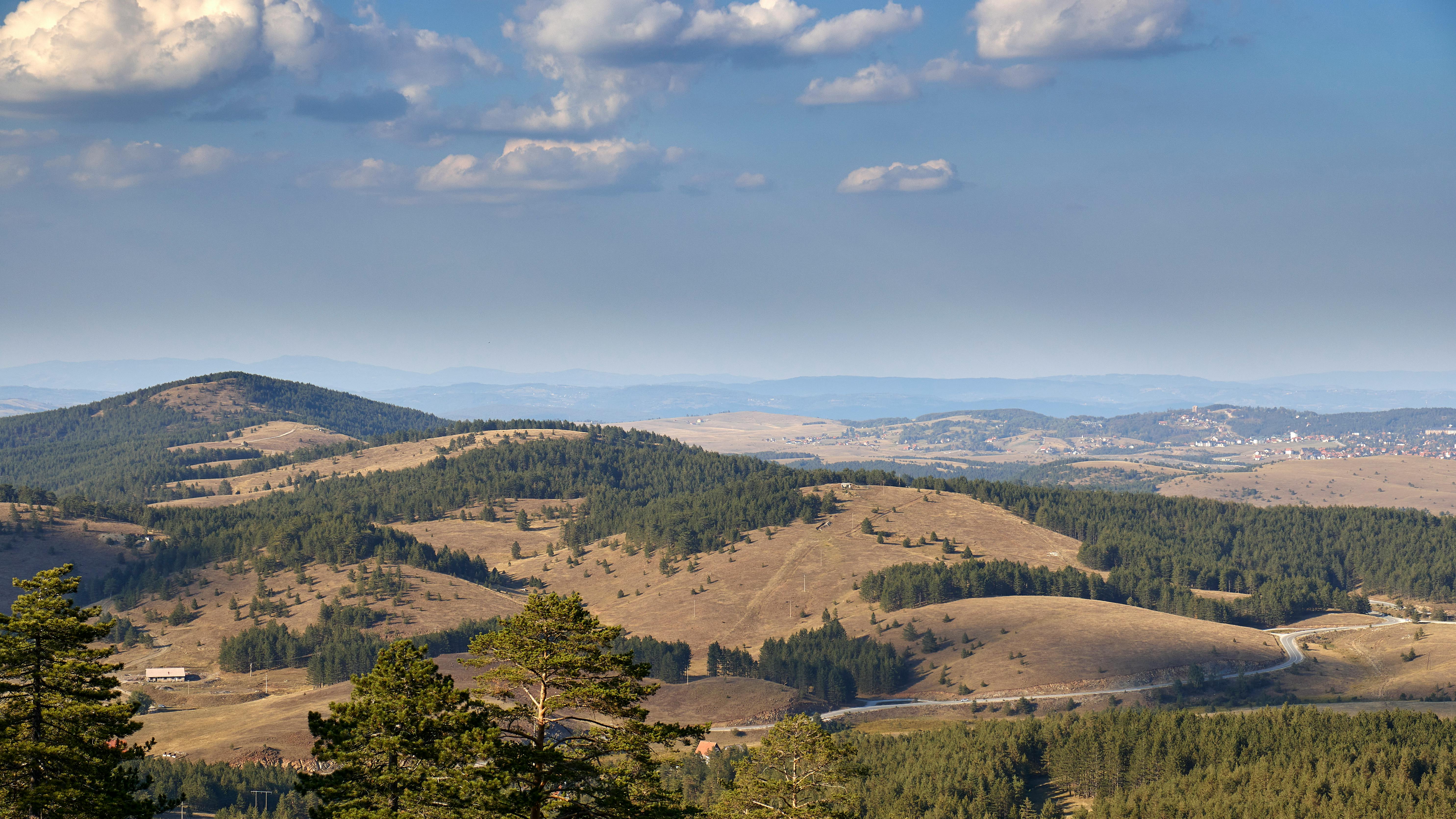 Aerial view of the rolling hills and forests of Zlatibor, Serbia, under a clear sky.