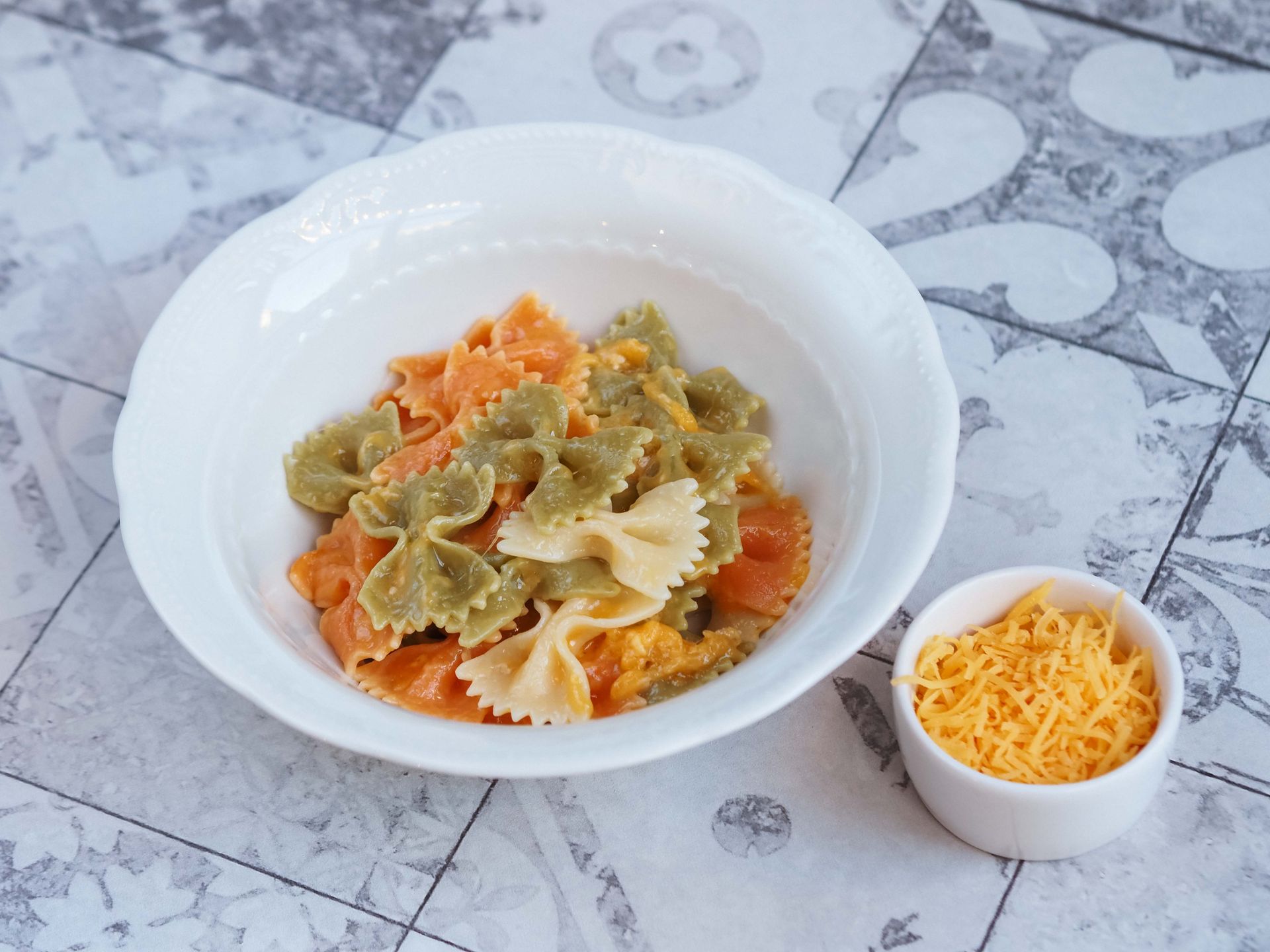 Vibrant tri-color farfalle pasta served with shredded cheese in a ceramic dish.