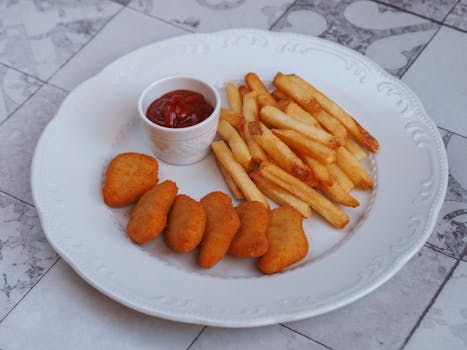 Delicious chicken nuggets with French fries and ketchup on a white plate.