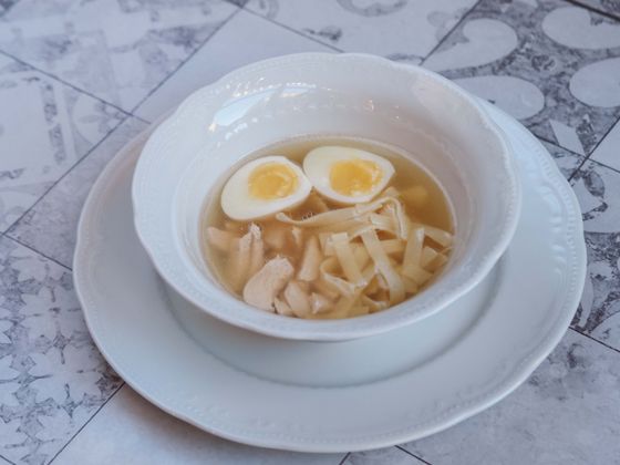 Clear golden chicken broth with flat egg noodles, shredded chicken and two halved boiled eggs