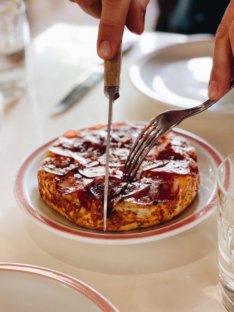 Hands Cutting A Small Pizza On Plate With Fork And Knife 