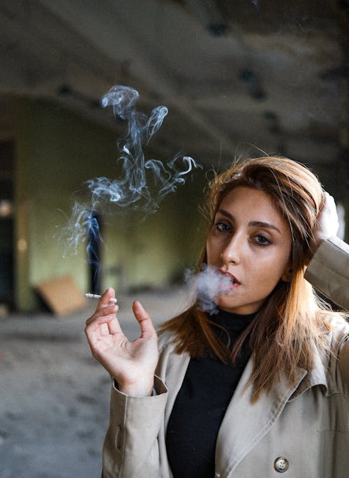 Woman Wearing a Beige Coat Smoking a Cigarette