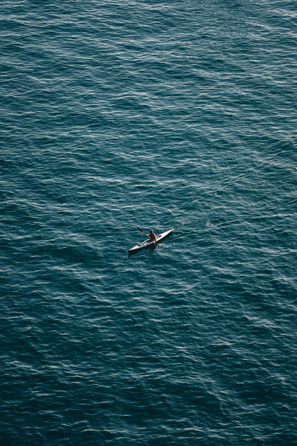 Solitary kayaker paddling across vast open water under clear sky
