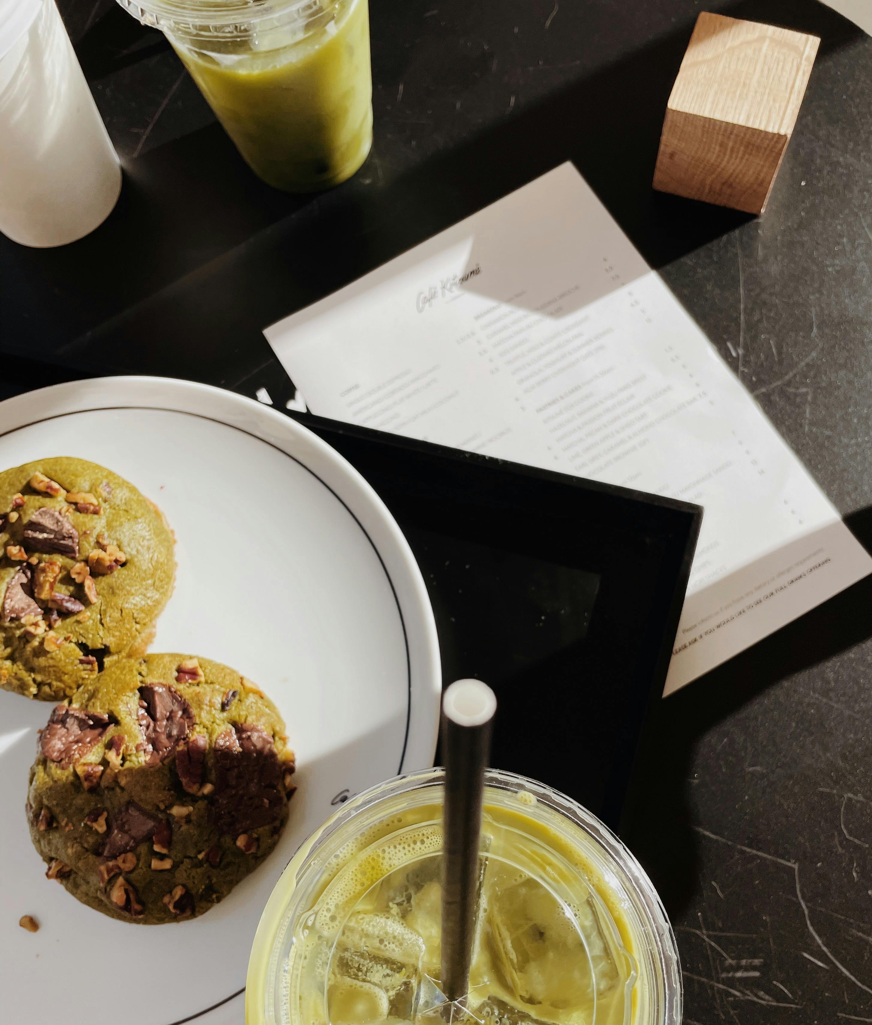 Top view of matcha cookies and a refreshing drink on a dark countertop, capturing a casual café setting.