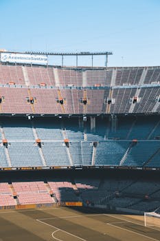 An empty soccer stadium with tiered seating under a clear blue sky, capturing shadows and sunlight.