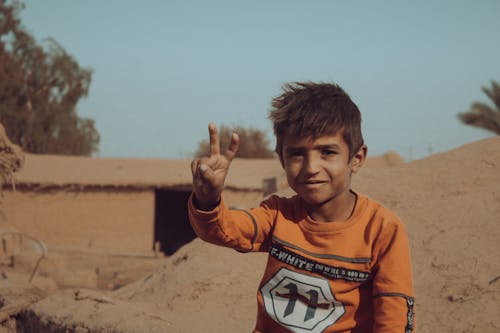 Close-Up Shot of a Boy in Orange Long Sleeve Making a Peace Sign