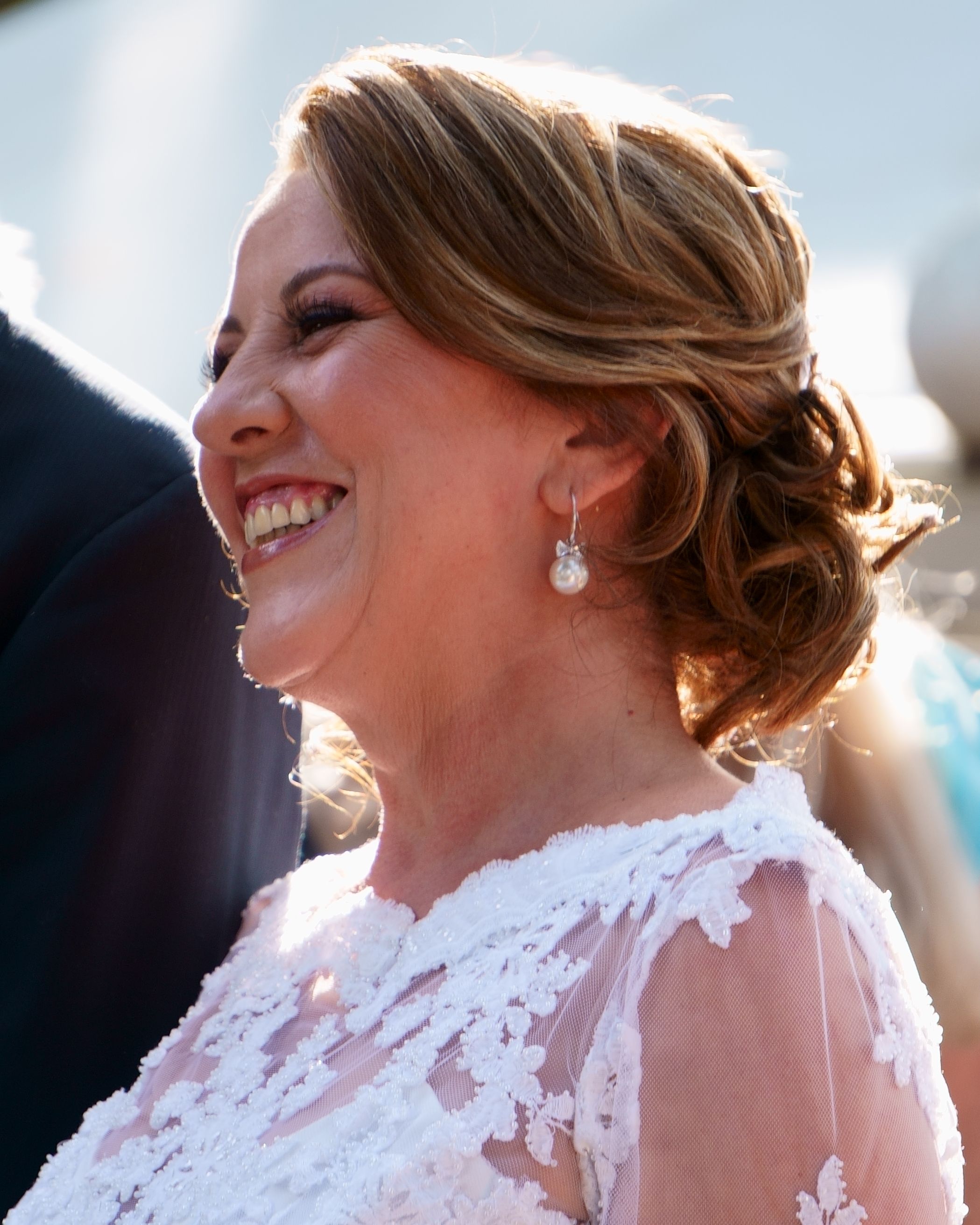 Side view portrait of a woman smiling in an elegant lace dress outdoors.