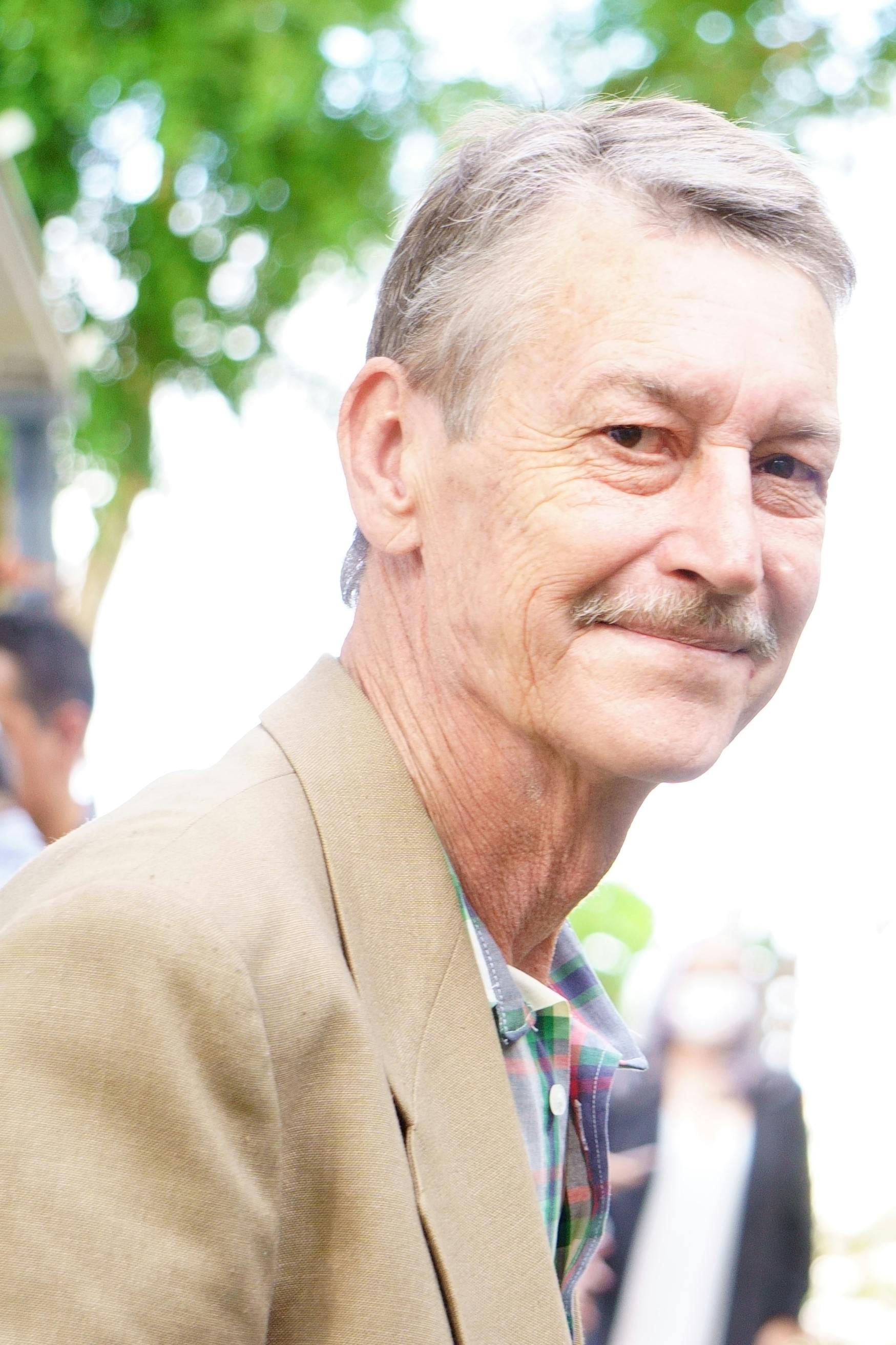 Portrait of a senior man smiling in the sunlight with a blurred outdoor background.