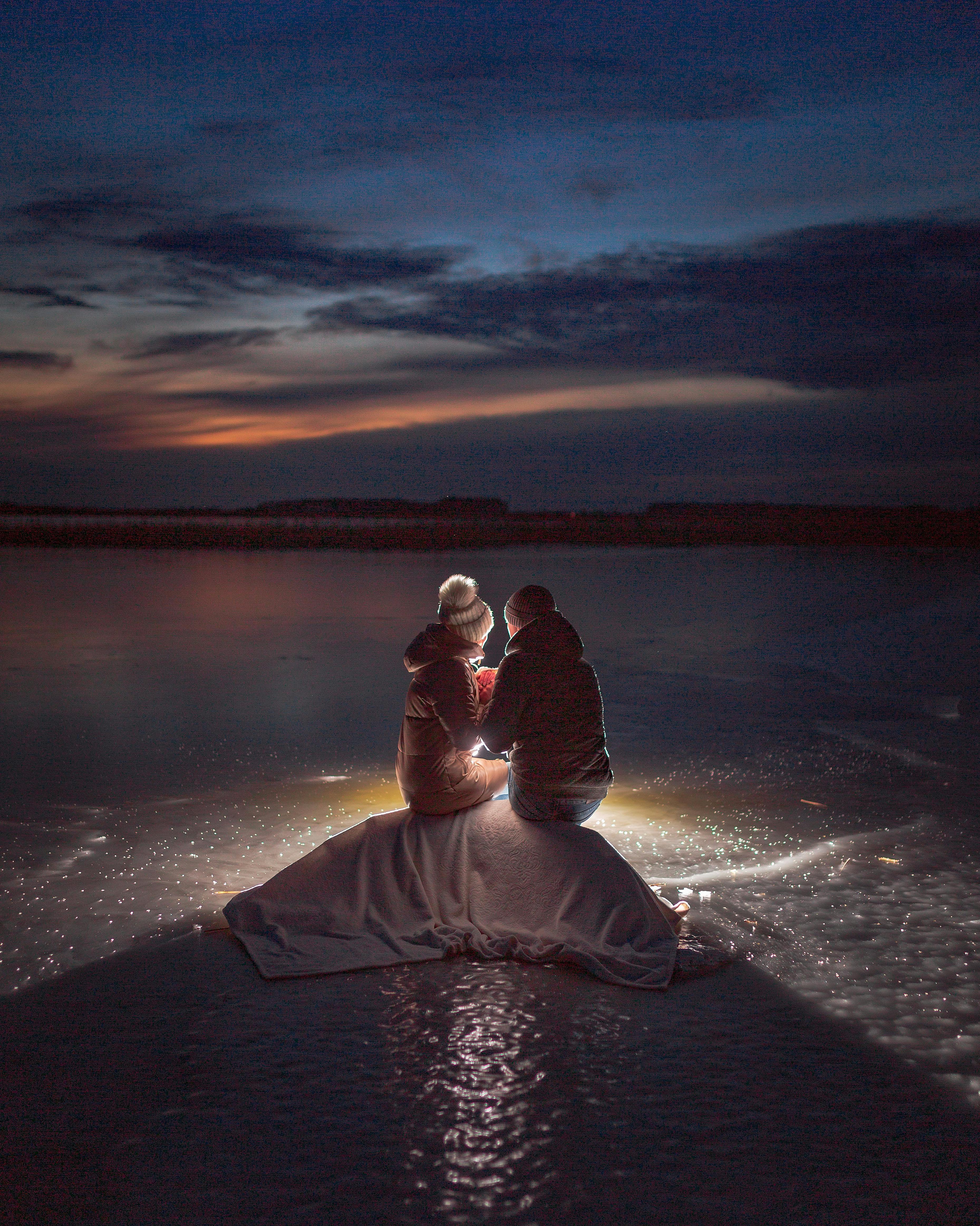 Couple enjoying a cozy night on a frozen, illuminated lake under a starlit winter sky.
