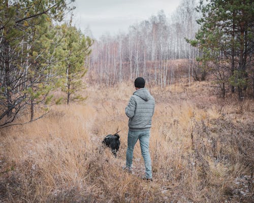 Man in Gray Jacket and Blue Denim Jeans Walking his Dog