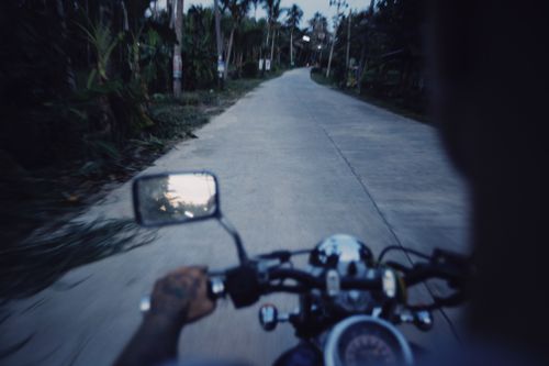 Free A motorcyclist drives through a rural road lined with trees at dusk, capturing adventure. Stock Photo