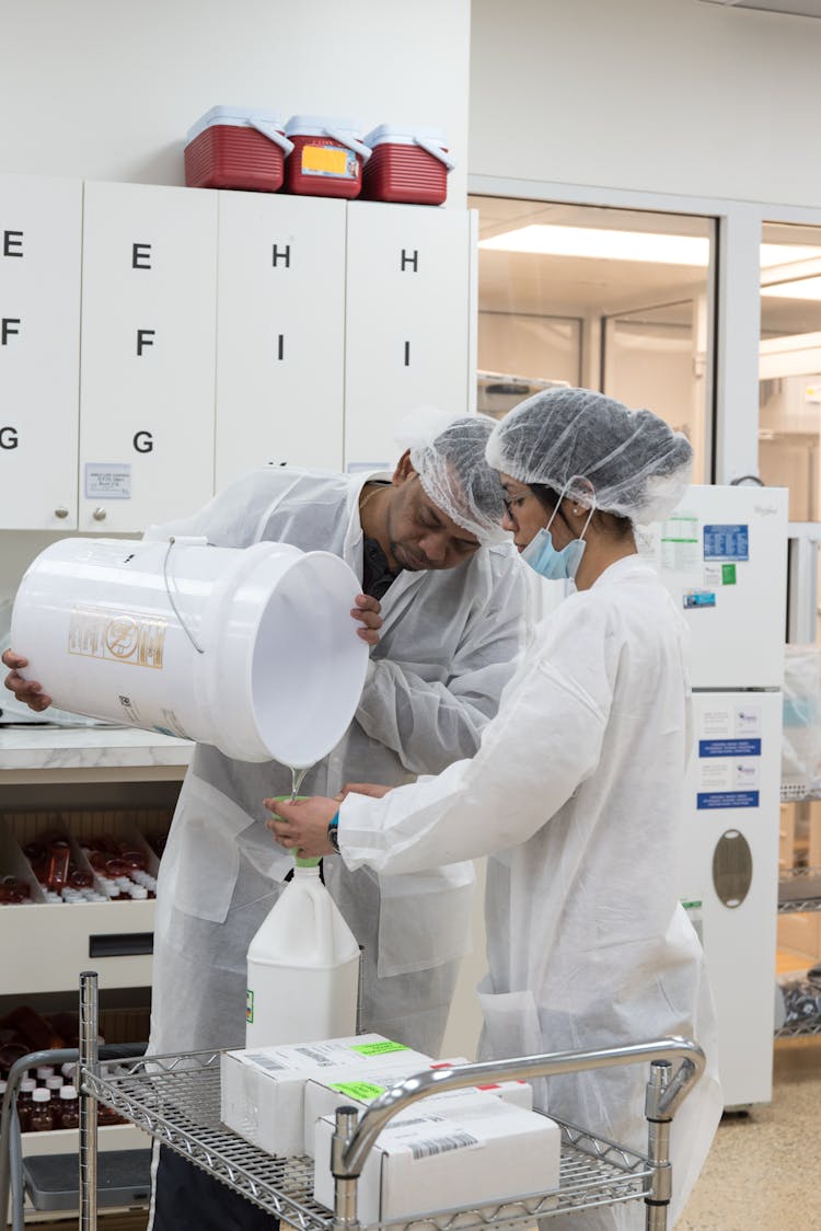 Ethnic Laboratory Workers Pouring Liquid From Bucket Into Bottle