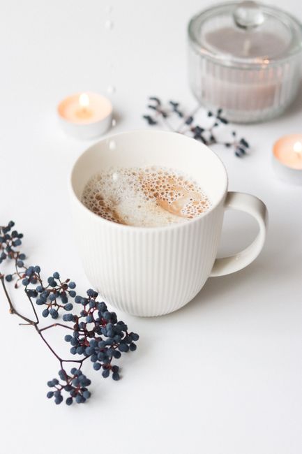 A serene scene of a coffee cup with blue berries and lit candles on a white table.