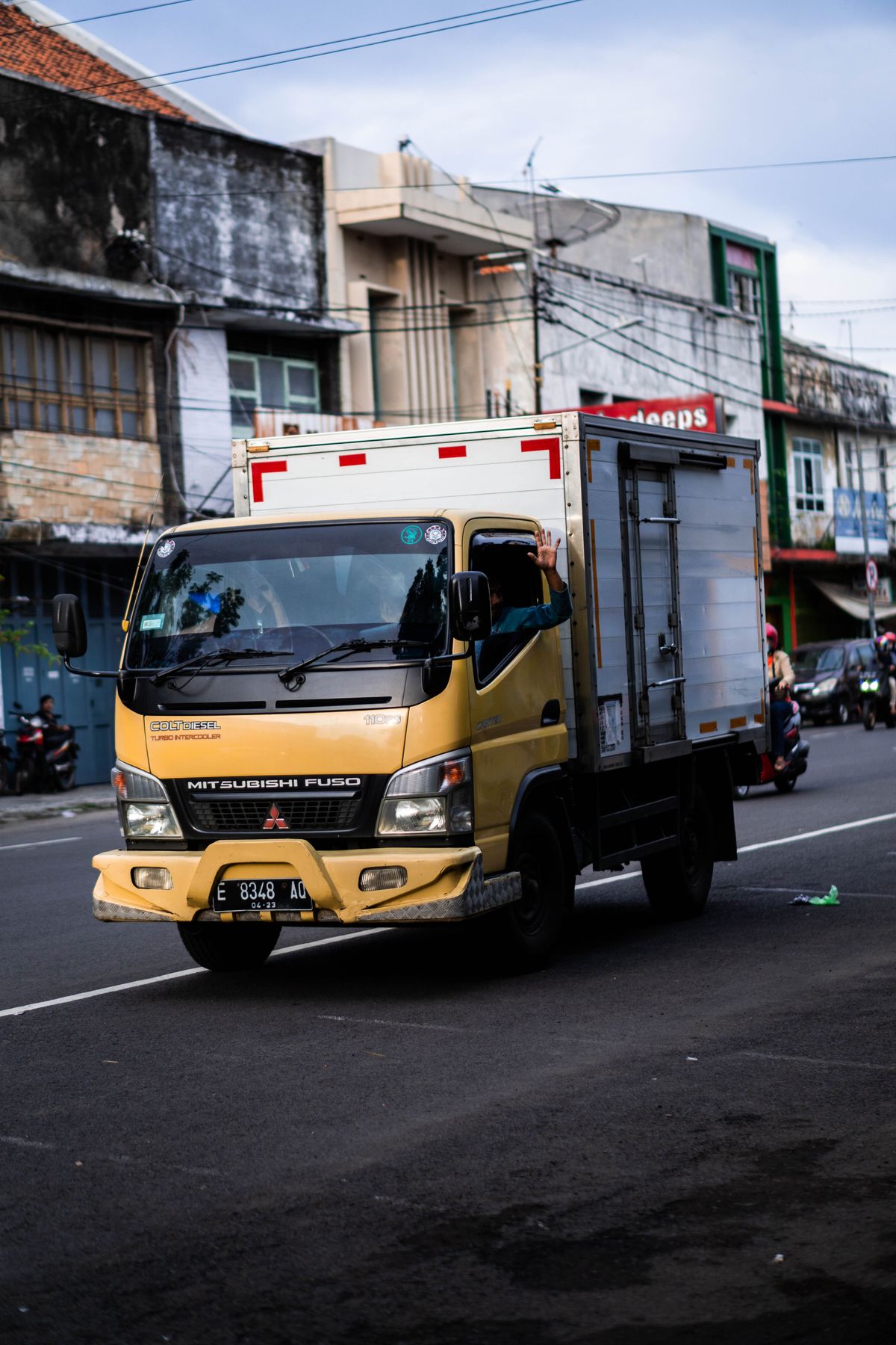 Yellow Mitsubishi Fuso lorry on a Southeast Asian city street — a daily working vehicle whose branding has to last without interrupting operations