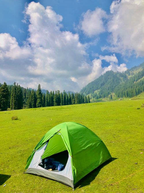 Free Green tent on a lush meadow with mountain backdrop and blue sky, ideal for outdoor enthusiasts. Stock Photo