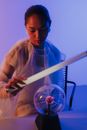 A Female Holding a Light Bulb Over a Plasma Ball 