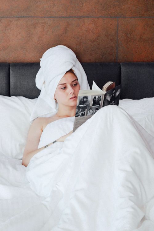 Free A woman wrapped in a towel reads a book in bed, exuding relaxation and self-care. Stock Photo