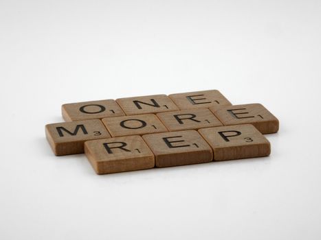 Scrabble tiles arranged to spell 'ONE MORE REP' on a clean white background.