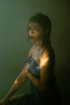 Moody portrait of a woman with wet hair wrapped in a towel, highlighted by dramatic lighting.
