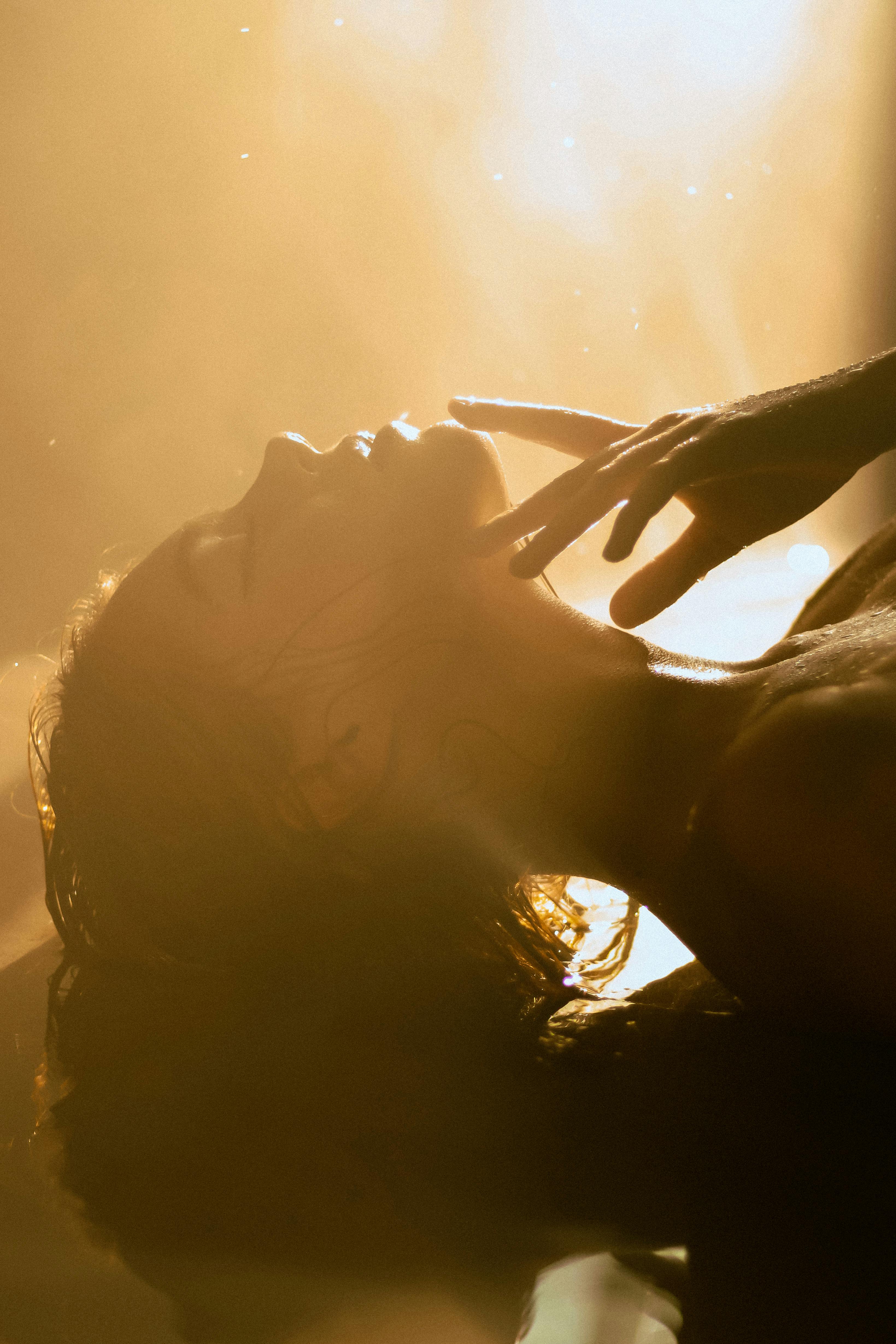 Artistic portrait of a woman basking in warm sunlight with eyes closed.