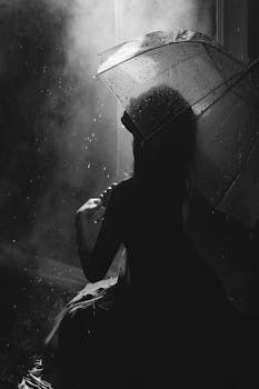 Artistic silhouette of a woman under an umbrella in the rain, captured in monochrome.