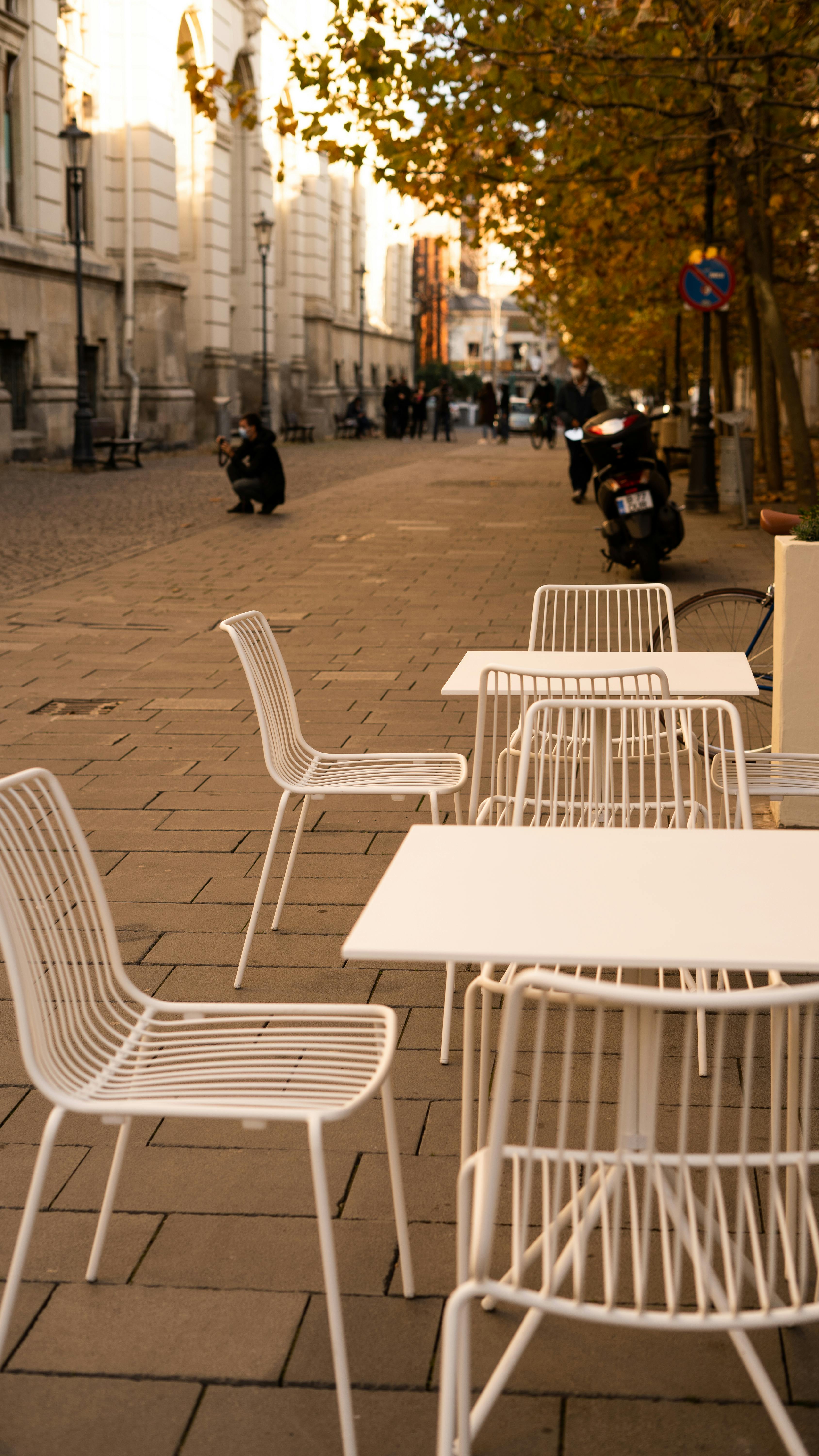 White chairs and tables on a București sidewalk in autumn, with a warm urban atmosphere.