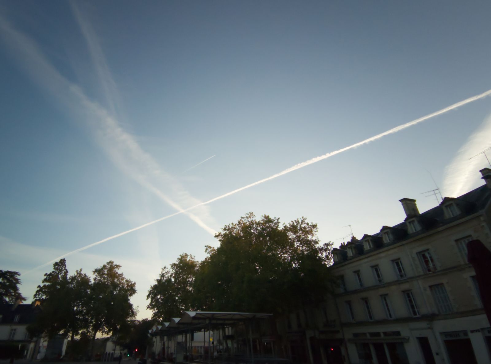Traînées d'avions croisées dans un ciel bleu au-dessus d'une place de ville