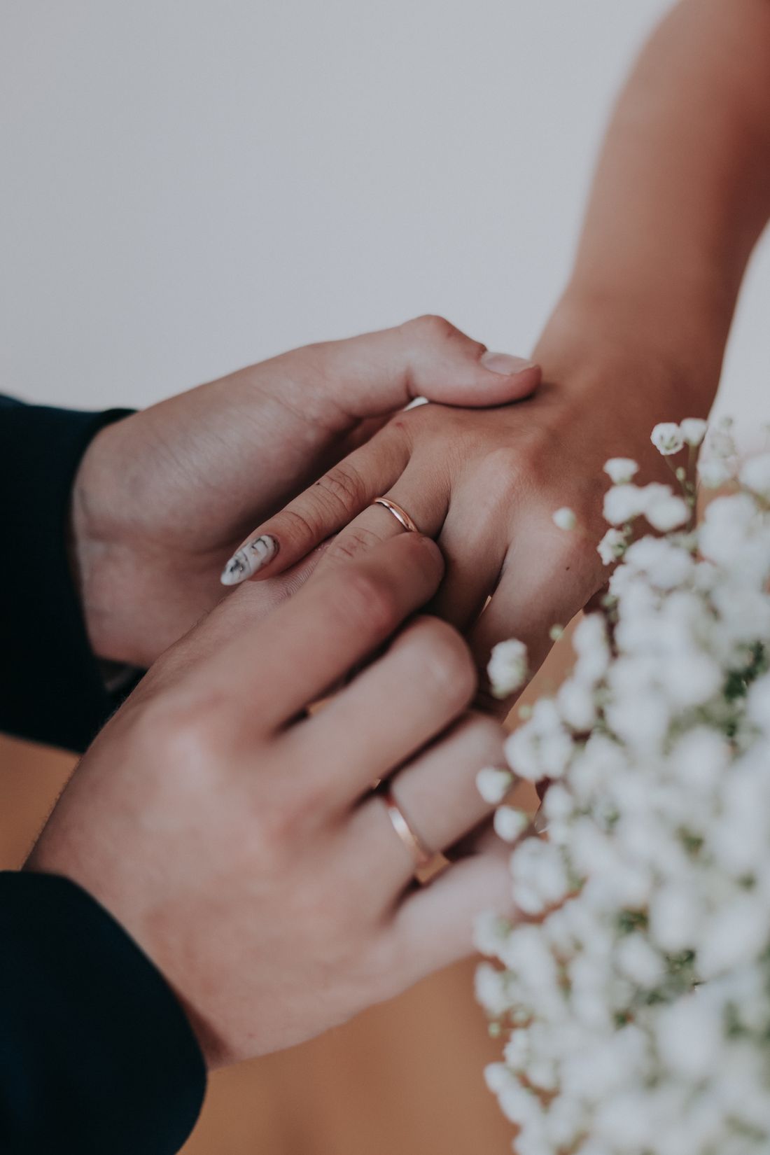 Two hands exchanging a wedding ring among delicate white flowers