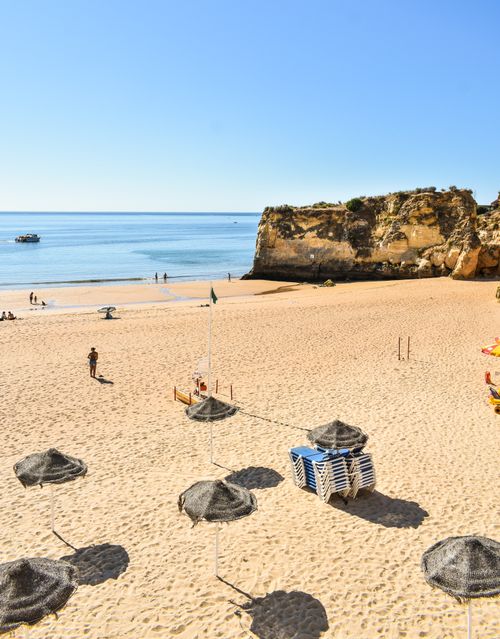 Free A sunny day at the beach with umbrellas, rocks, and a calm sea. Stock Photo