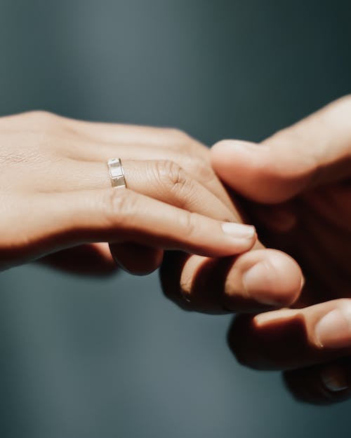 Free Close-up of hands exchanging a wedding ring on a soft green background. Stock Photo