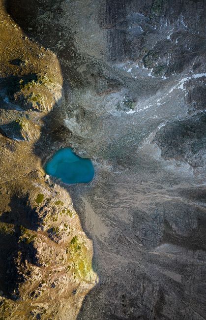 A breathtaking aerial view of a small mountain lake surrounded by rough rocky terrain, captured under natural sunlight.