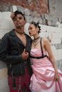 Man in Black Jacket and Plaid Pants Standing Beside a Woman in Pink Tube Dress with Black Lipstick