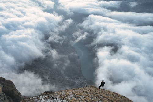 A Person Standing on the Mountain Peak Near the Clouds