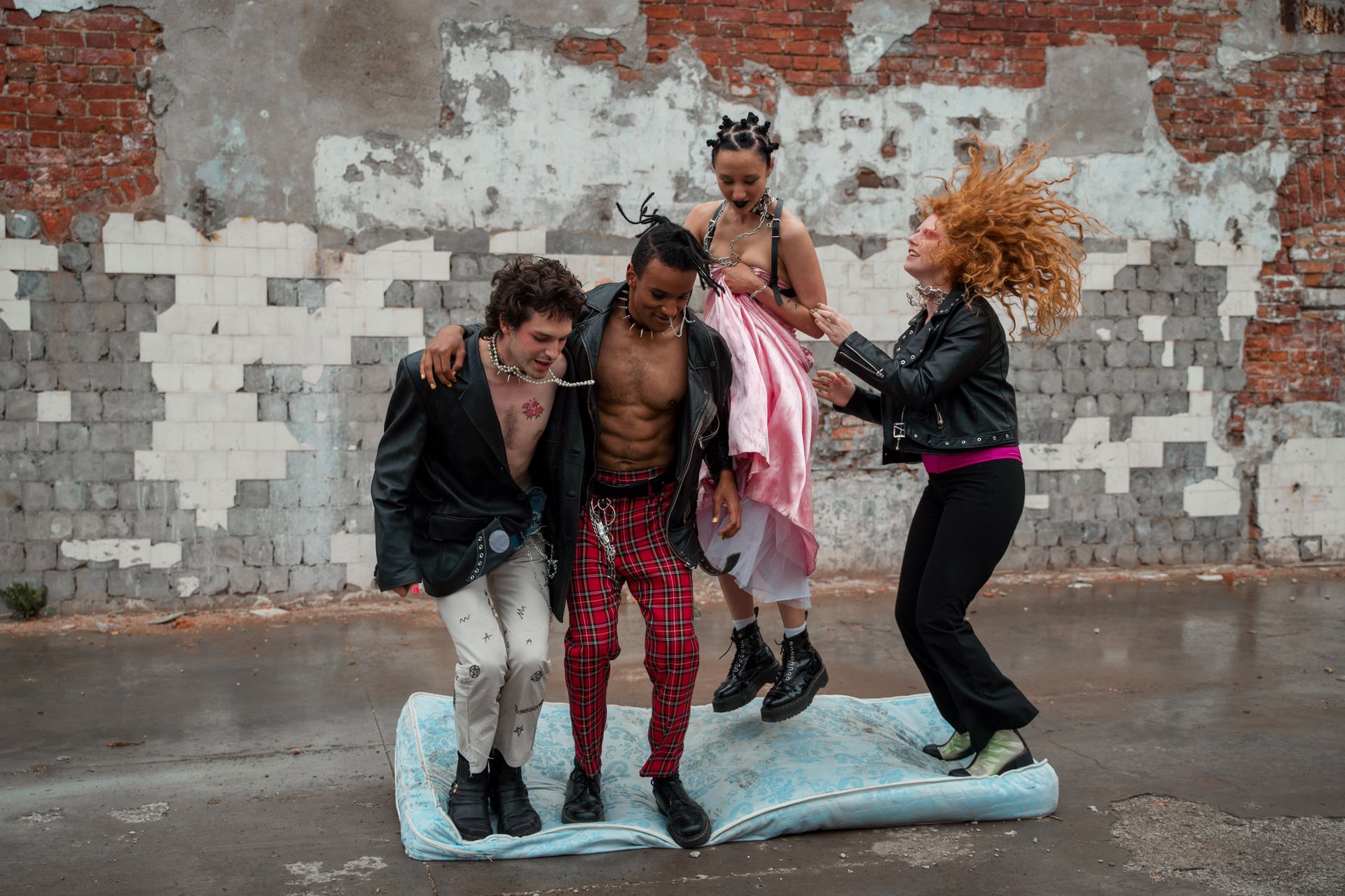 Energetic group in punk fashion jumping on a mattress in an urban setting. Vibrant and rebellious.
