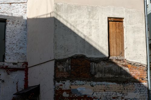 Free An abandoned building featuring a weathered brick wall and dramatic shadows, conveying urban decay. Stock Photo