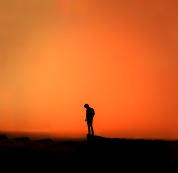 A lone silhouette stands against a vibrant orange sunset sky, evoking introspection.