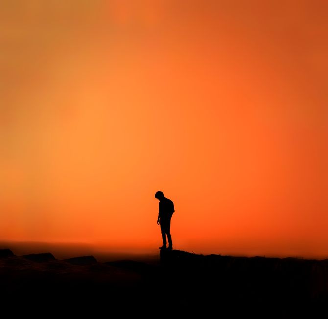 A lone silhouette stands against a vibrant orange sunset sky, evoking introspection.